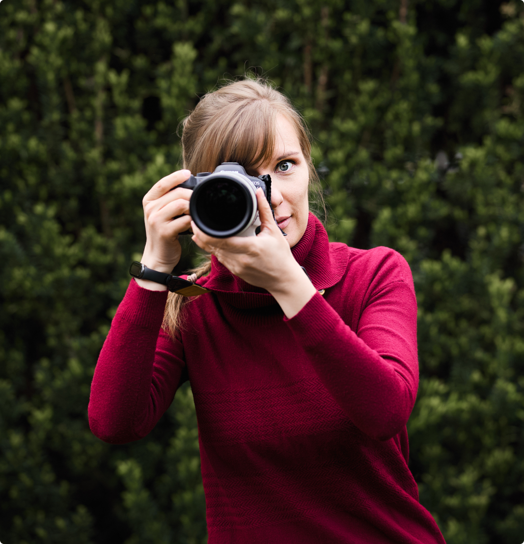 fotografka w bordowym swetrze celująca obiektywem w odbiorcę